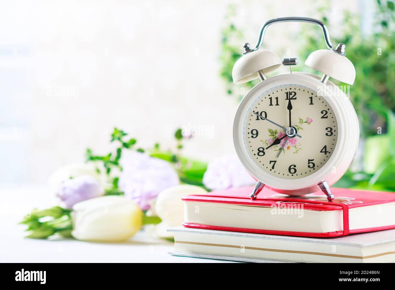 Retro alarm clock, notebook and spring flowers. Stock Photo