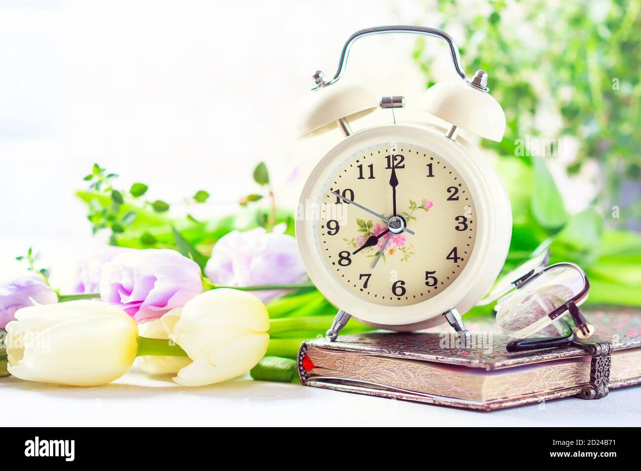 Retro alarm clock, notebook and spring flowers. Stock Photo