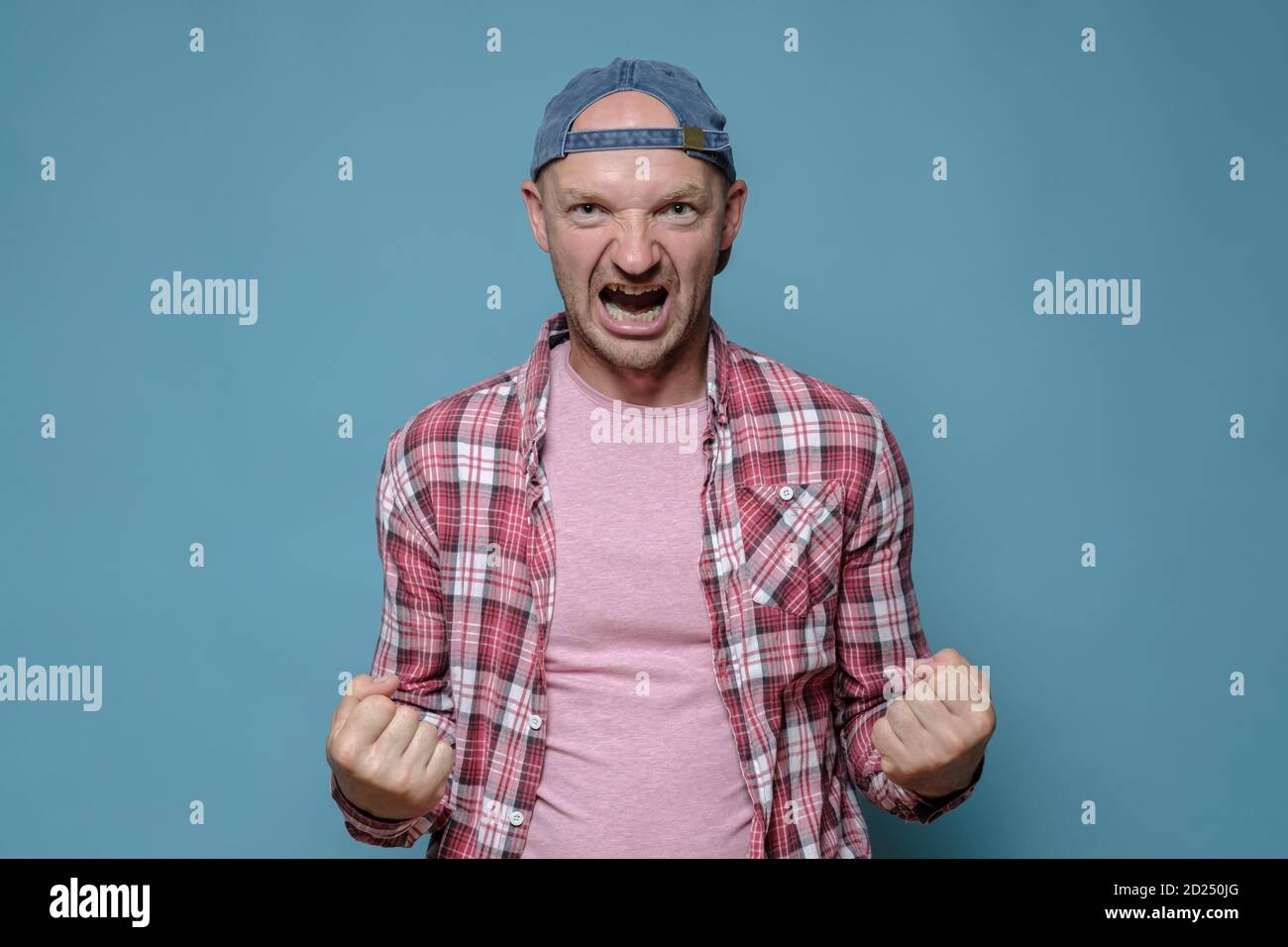 Caucasian man threatens someone, he clenched his fists showing his strength and shouts furiously. Blue background. Stock Photo