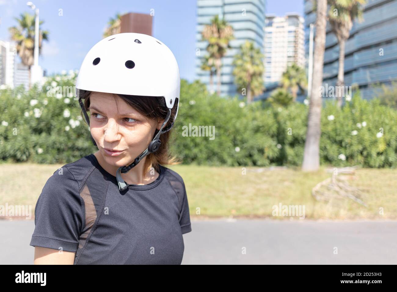 Young roller skater caucasian woman in the white helmet and black sporty clothes on a sunny day in the skatepark, urban environment Stock Photo