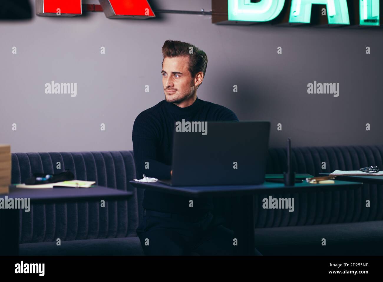 Young businessman sitting at a desk in a shared office space looking deep in thought and working on a laptop Stock Photo