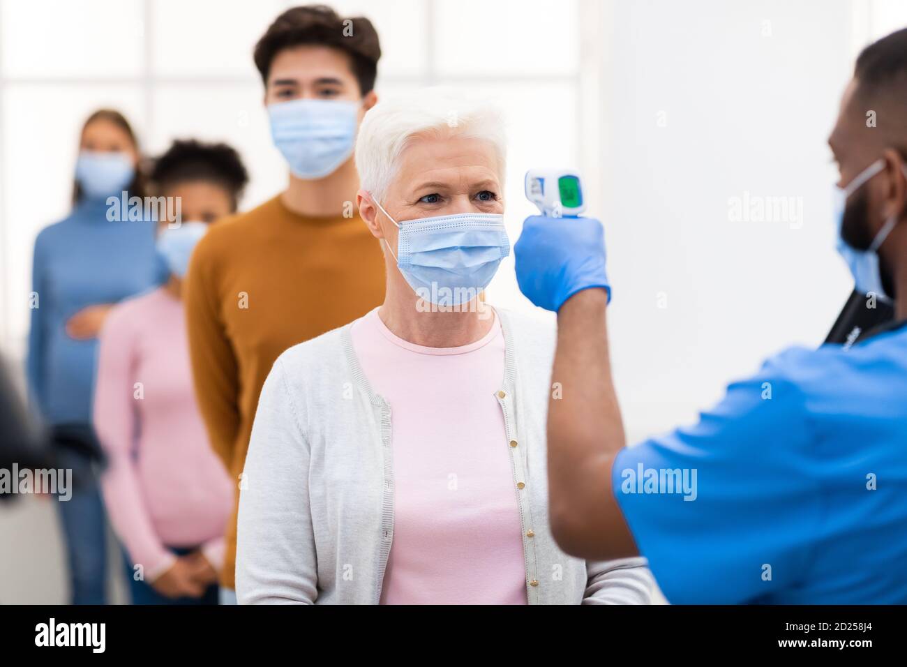 Worker Doing Temperature Screening Scanning Lady's Forehead With Themometer Indoors Stock Photo