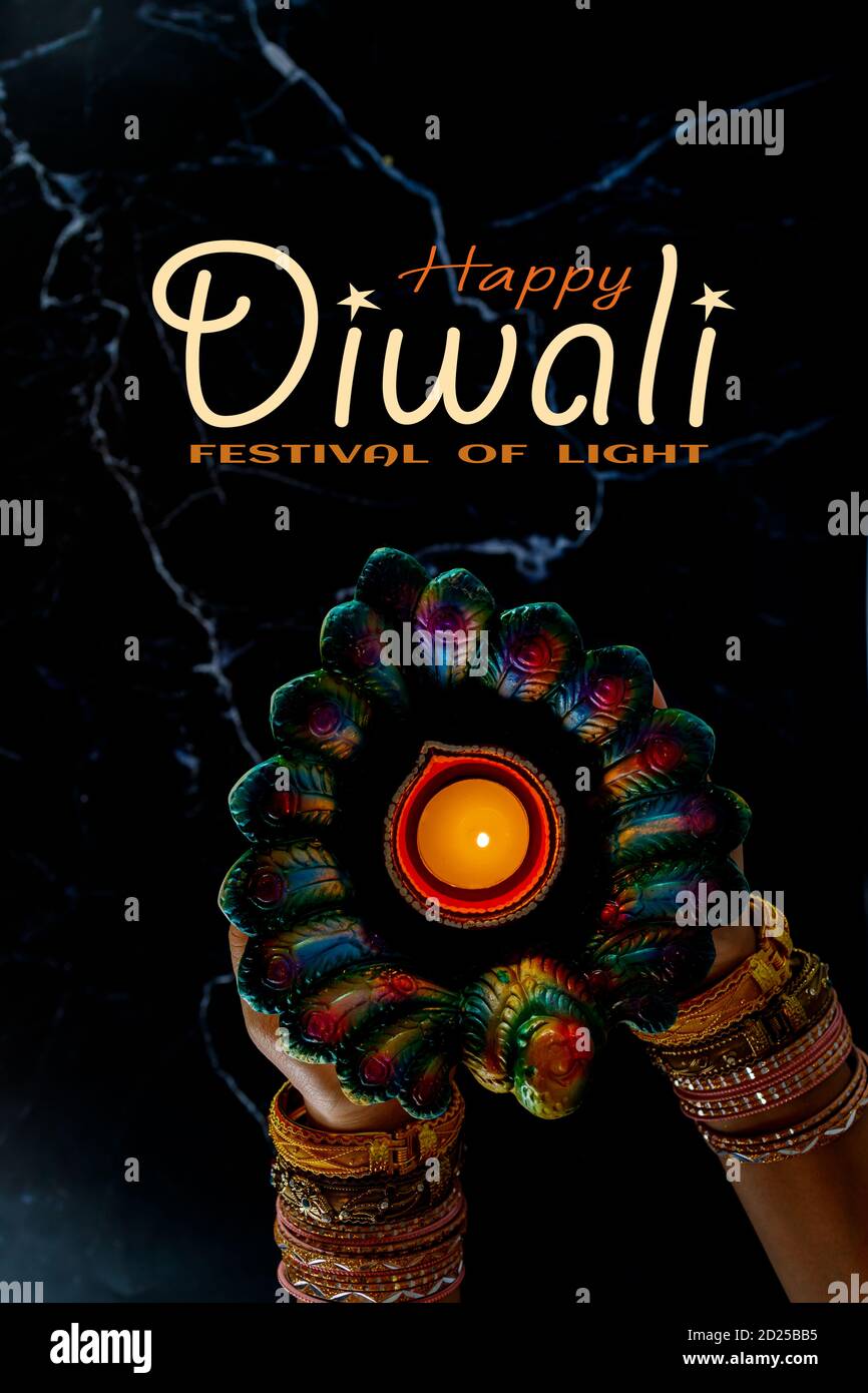 Happy Diwali - Woman hands with henna holding lit candle isolated on dark background. Clay Diya lamps lit during Dipavali, Hindu festival of lights ce Stock Photo