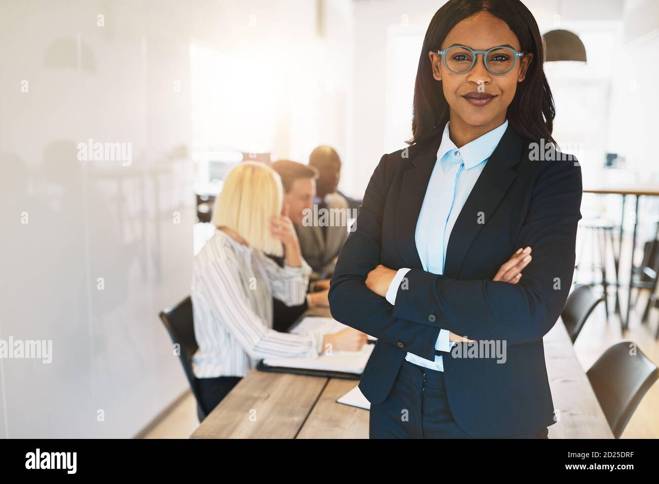 Smiling young African businesswoman standing with her arms crossed in ...