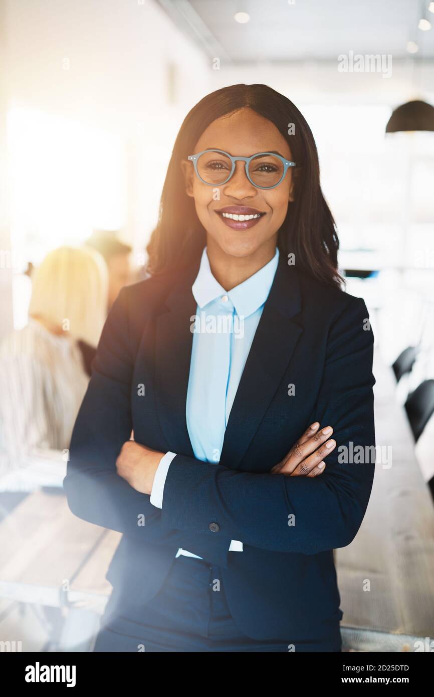 Smiling young African businesswoman standing with her arms crossed in ...