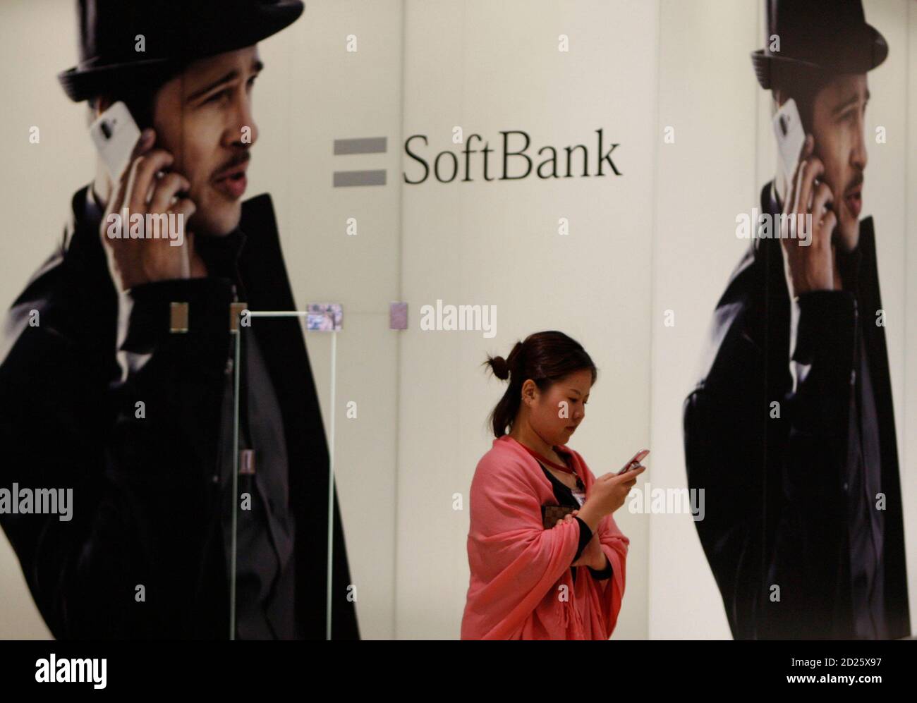 A woman using a mobile phone walks past an advertisement board of Softbank Corp in Tokyo February 5, 2009. Softbank Corp, Japan's No.3 mobile phone operator, posted a 2.4 percent rise in quarterly profit as a drop in cellphone sales lowered its subsidy payments, and it stuck to its full-year forecast.   REUTERS/Toru Hanai (JAPAN) Stock Photo
