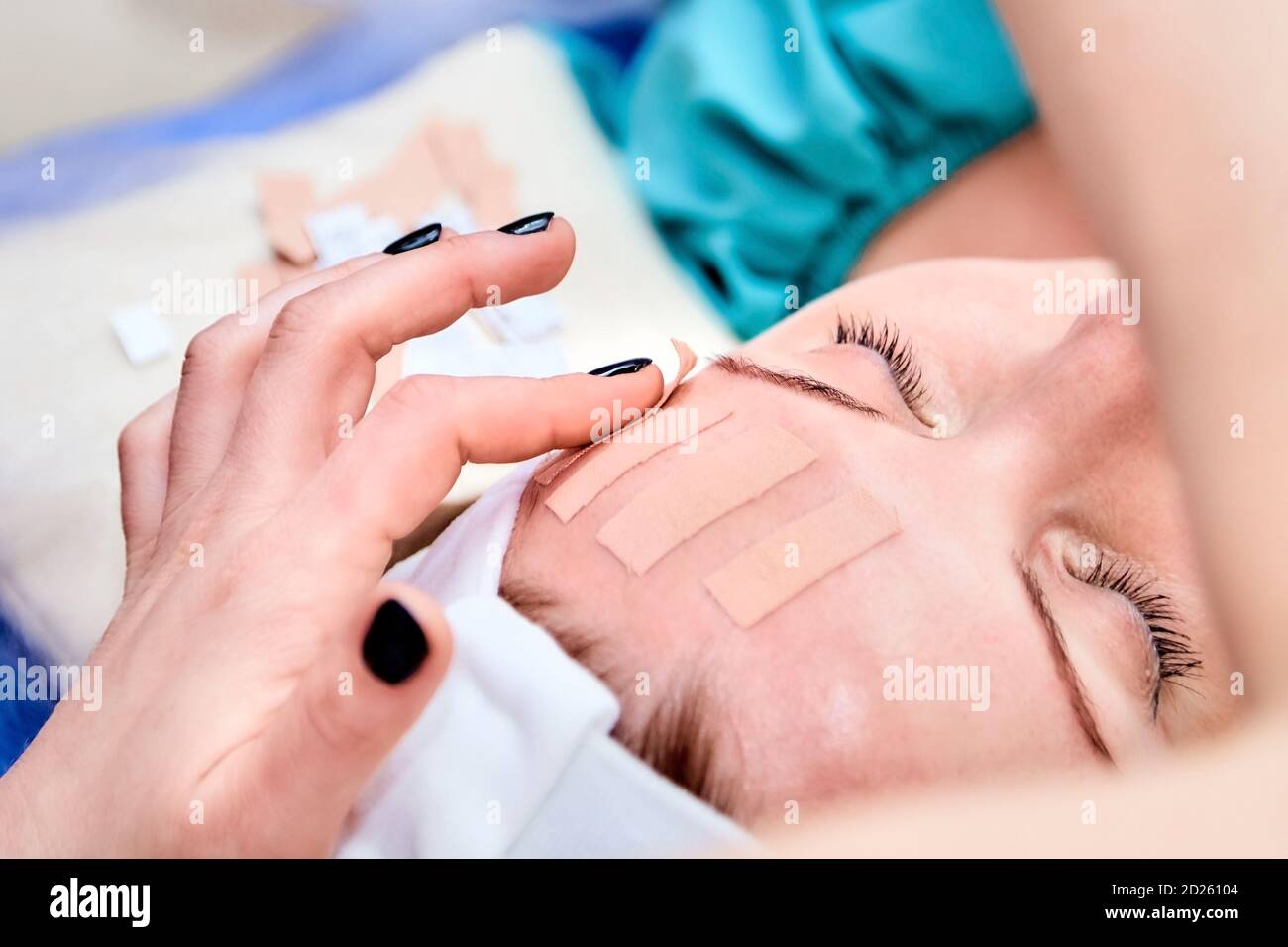 Facial skincare. Cosmetology procedure: Taping. Beautician sticks tape on the forehead of a woman. Cosmetologist hands Stock Photo