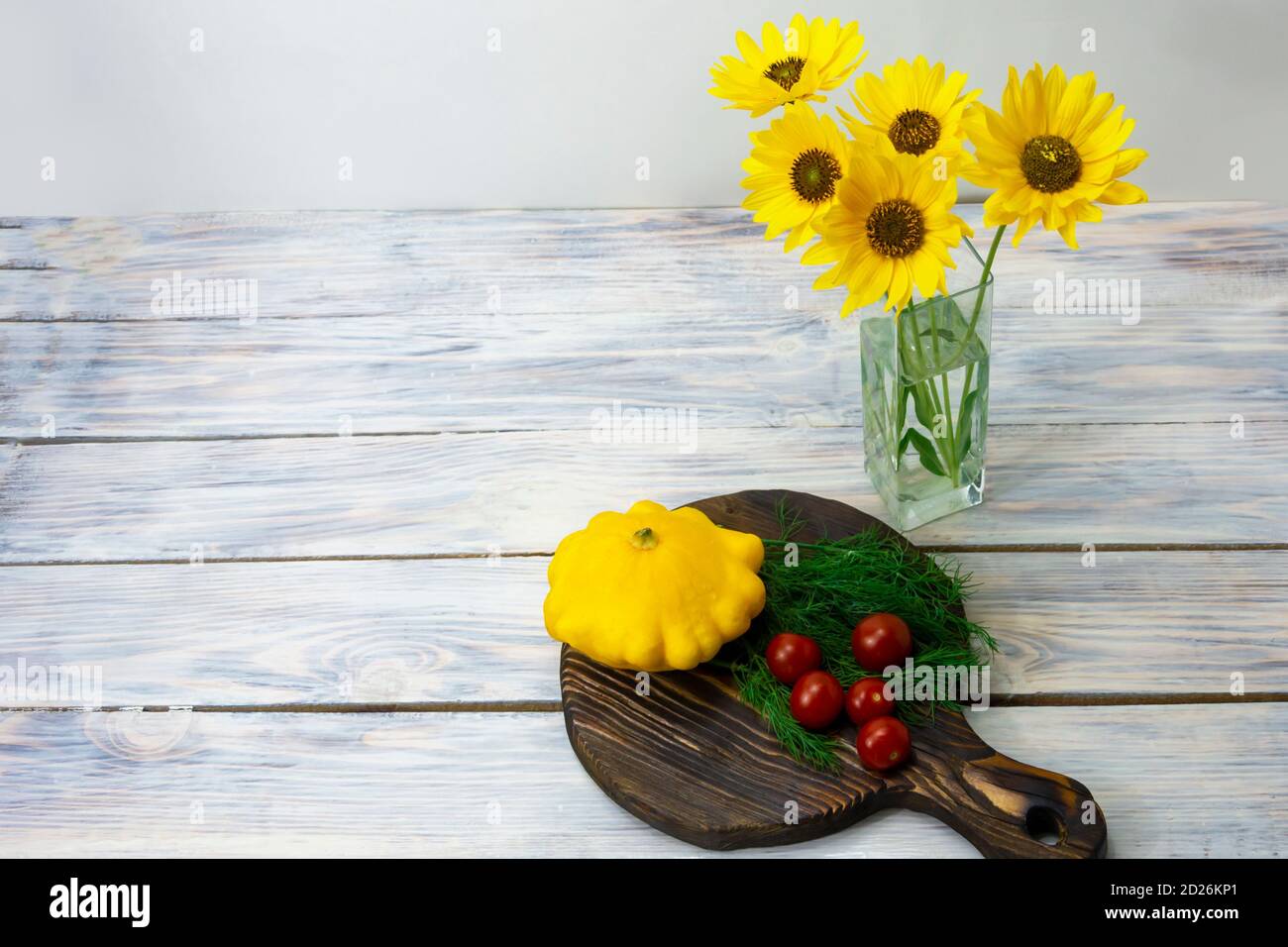 Yellow flowers in glass vase on wooden table with colorful vegetables