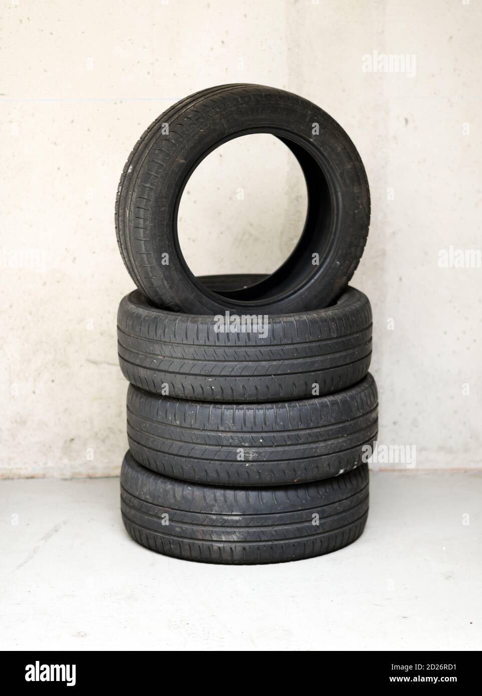Stack of four old used vehicle tyres in a garage or workshop with the top tyre balancing upended on the others against a wall with copy space below Stock Photo