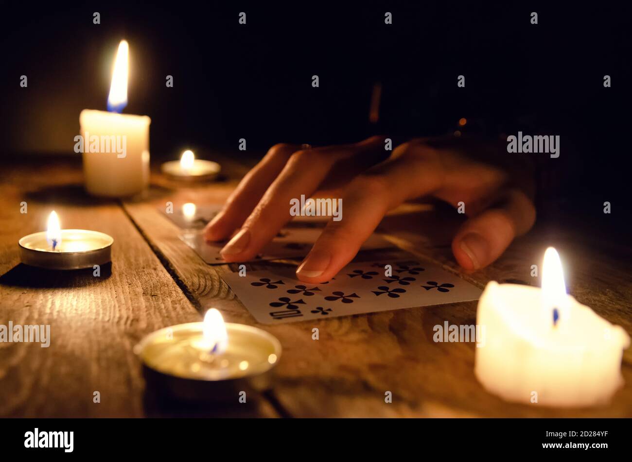 Hands of a fortune teller and cards on the table, around lit candles in the dark on a wooden table. concept of divination, magic Stock Photo