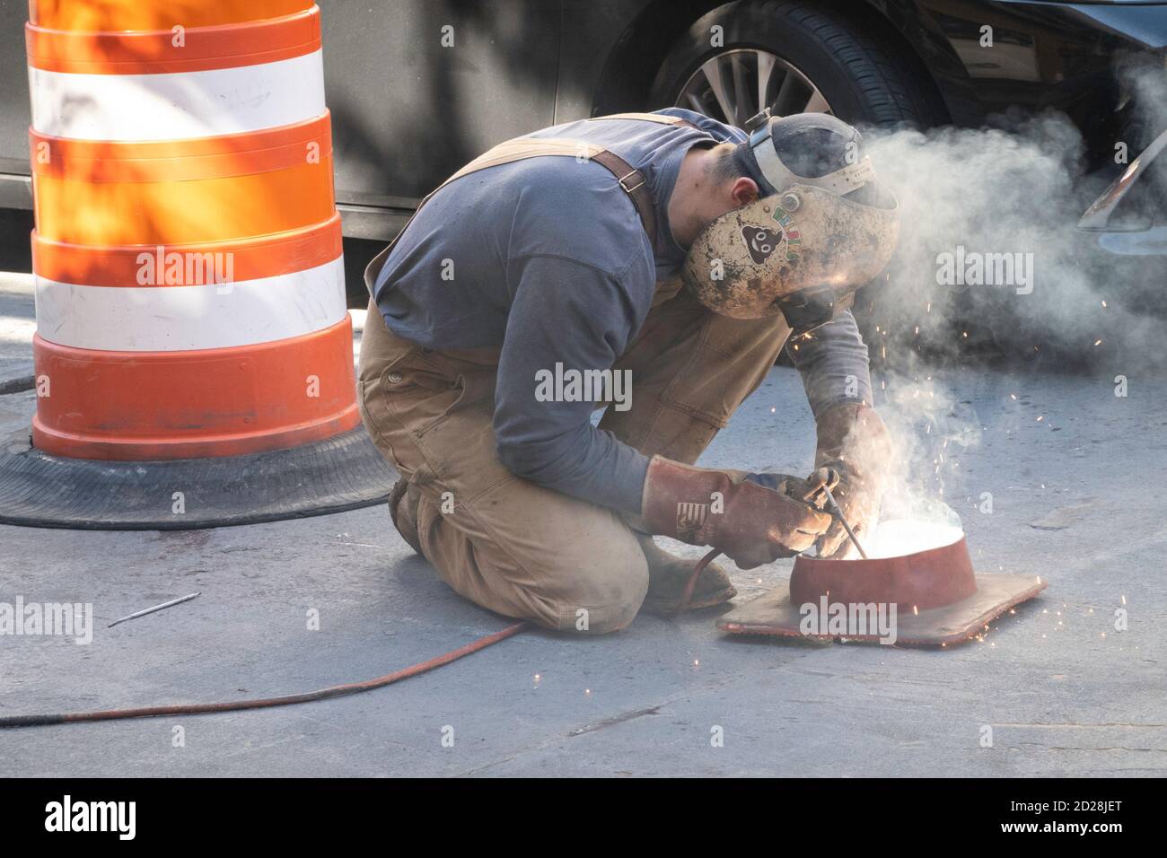 Worker welding steel plate on street, NYC Stock Photo