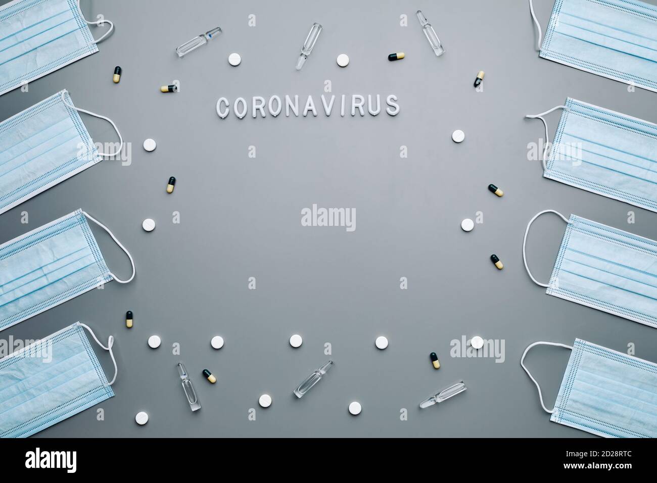 Above view composition of medical masks framing coronavirus word and medication laid out over grey background, copy space Stock Photo