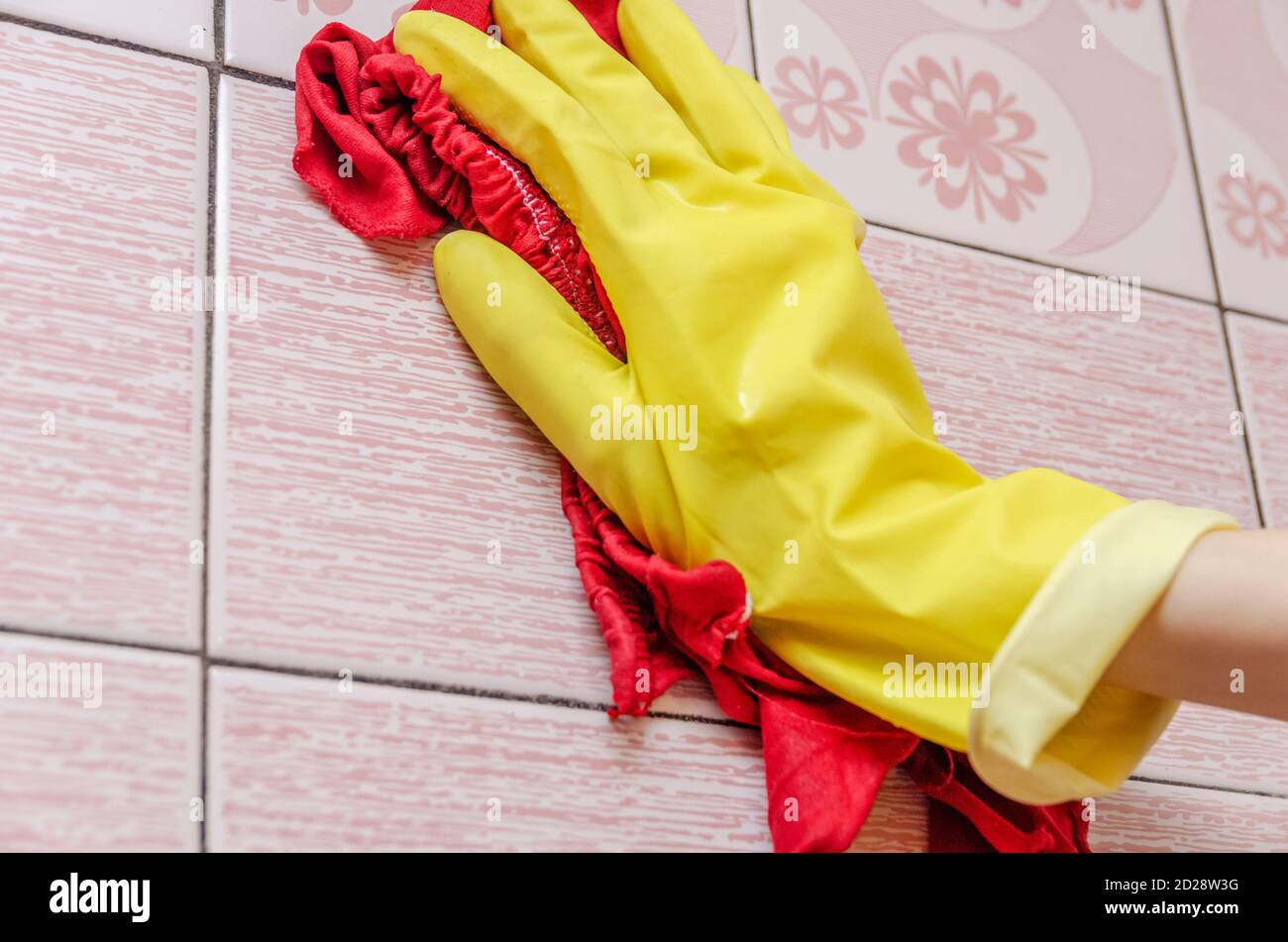 Female hand in a yellow glove with a red rag cleans a tile in a ...