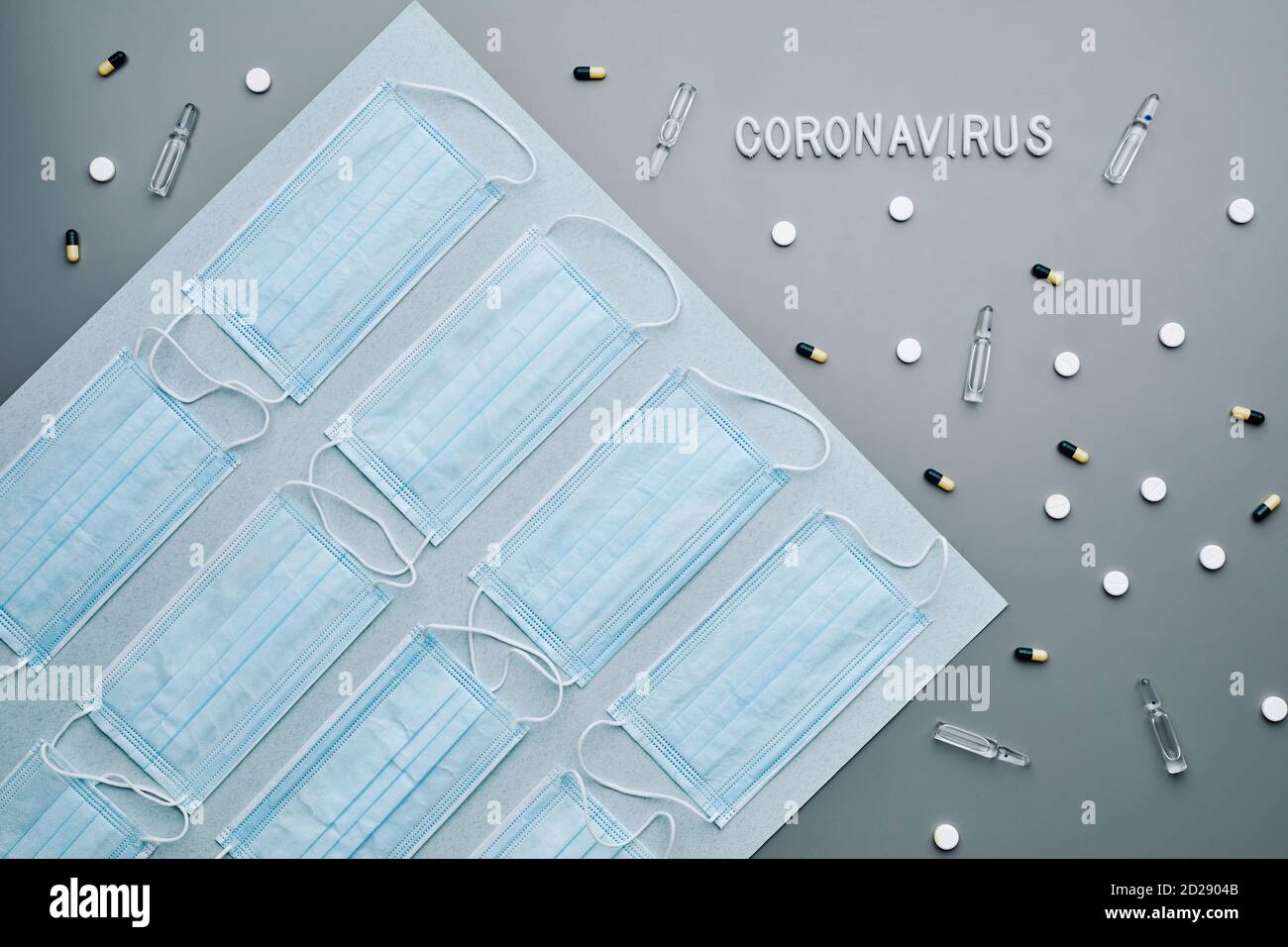 Top view composition of medical masks with coronavirus word and medication laid out in pattern over grey background, copy space Stock Photo