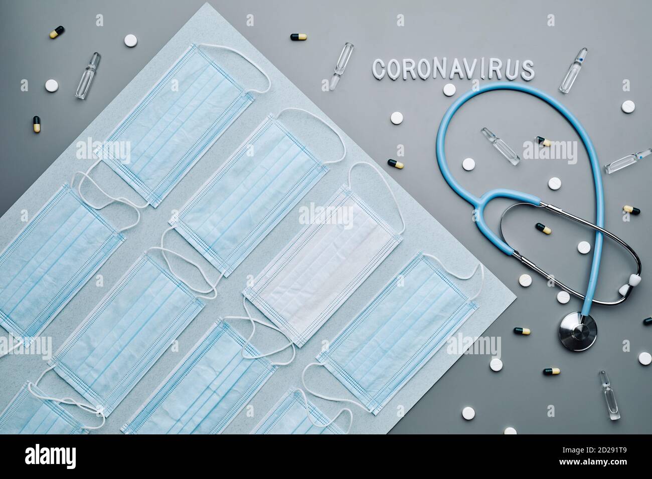 Top down composition of medical masks with coronavirus word and sthetoscope laid out over grey background, copy space Stock Photo