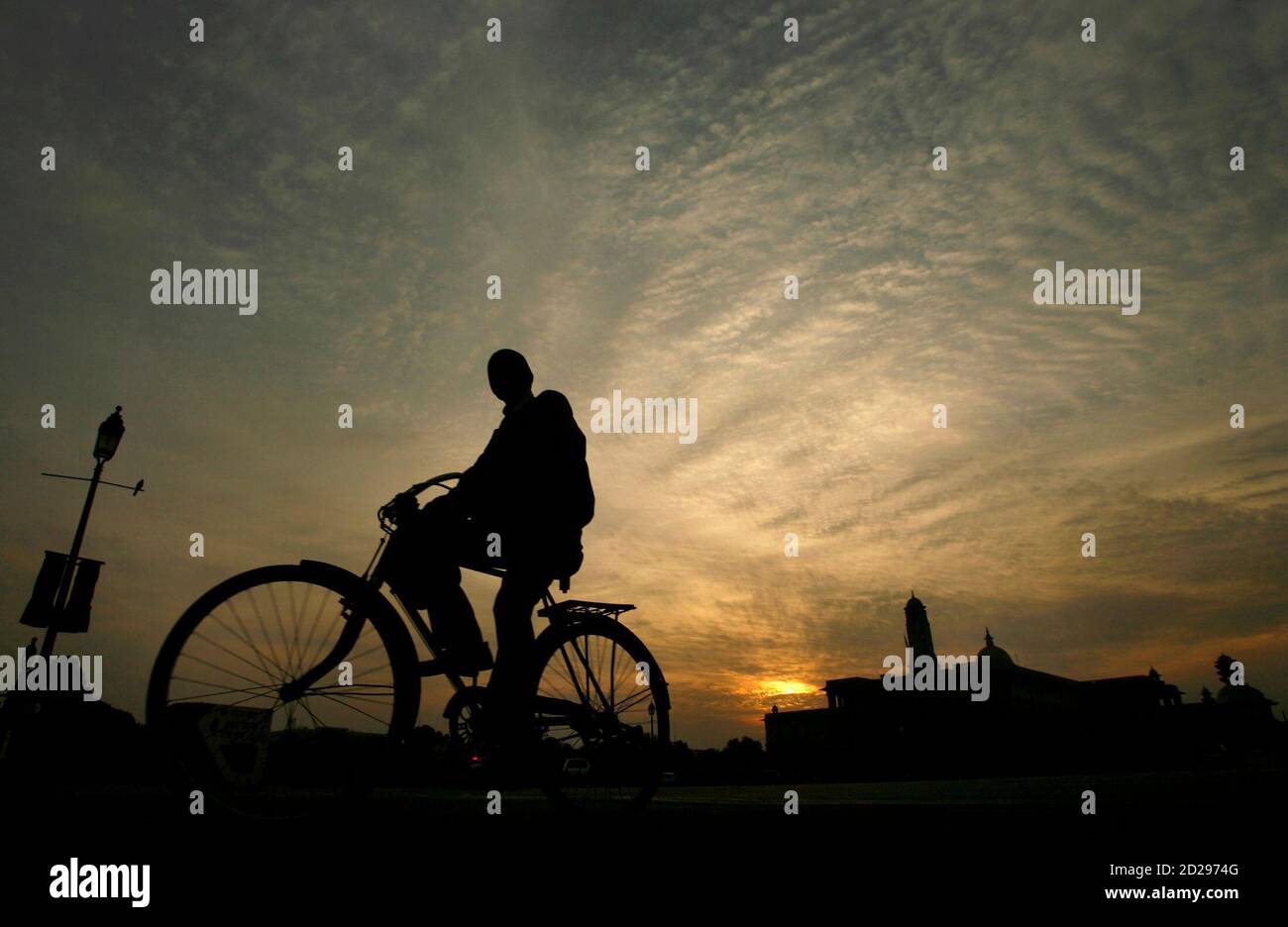 A man is silhouetted against the setting sun as he cycles past the Defence Ministry building in New Delhi December 31, 2007. REUTERS/Adnan Abidi (INDIA) Stock Photo