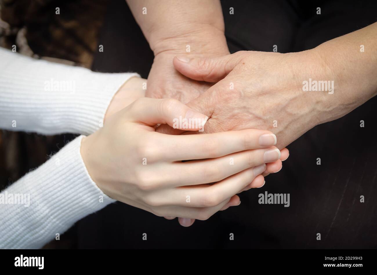 Hands of a young girl holding the hands of an old, elderly woman close ...