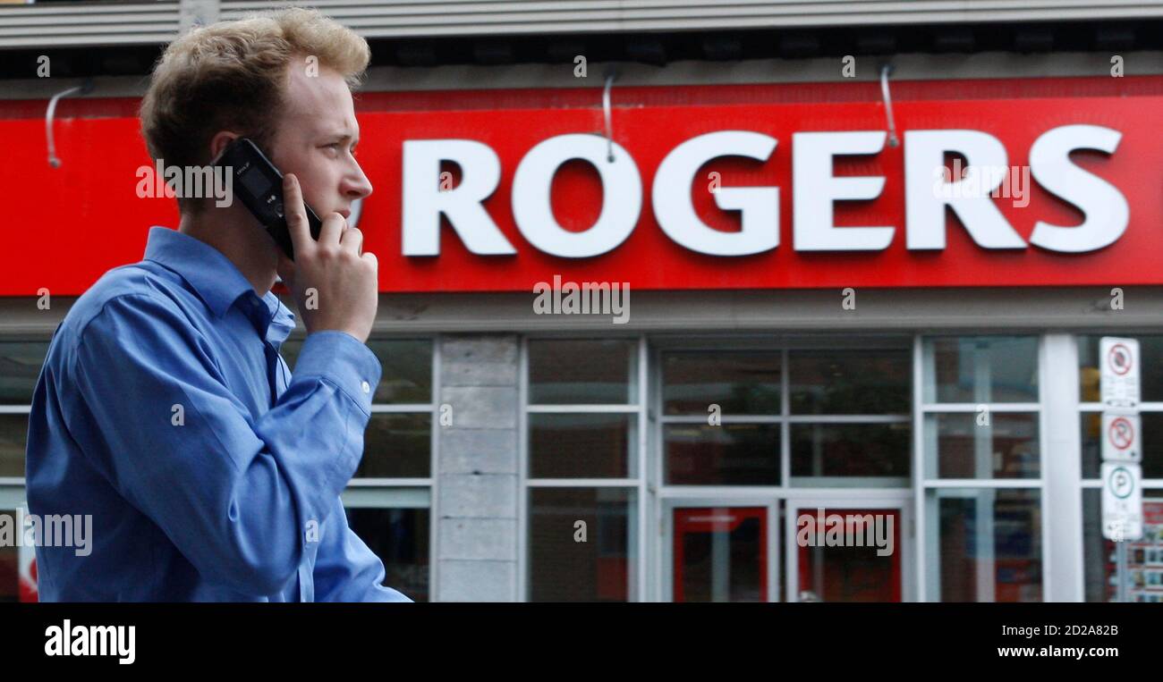 A pedestrian uses his mobile phone while walking past a Rogers store in Ottawa July 21, 2008. Canada's auction of wireless spectrum ended on Monday and new players appear poised to enter the market and challenge the country's Big Three carriers in a fight for mobile phone subscribers.        REUTERS/Chris Wattie       (CANADA) Stock Photo