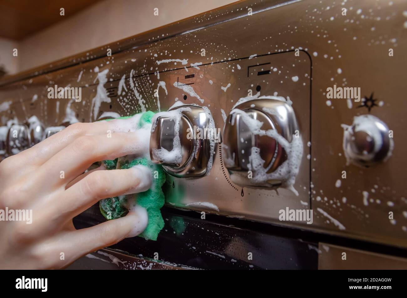 woman's hand washes a green sponge with foam on the switch handle of a gray stainless steel gas