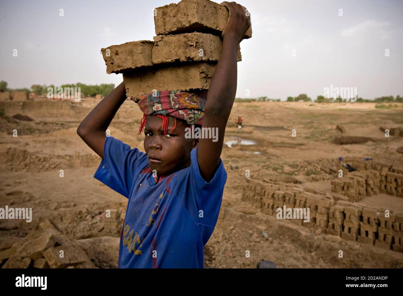 A boy carries bricks on his head at a riverside factory where mud is fired in kilns to produce building materials on the outskirts of Chad's capital N'Djamena, May 31 2008. Many children are used as cheap labour transporting bricks. REUTERS/Finbarr O'Reilly (CHAD) Stock Photo