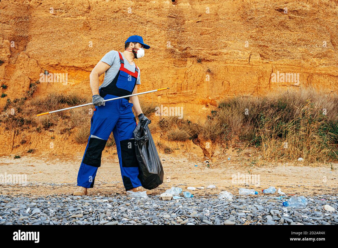 Man volunteer collecting garbage on the beach with a reach extender ...