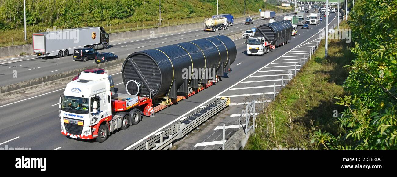 Looking down on wide oversize long cylinder shape load on haulage lorries & trucks with low loader trailer occupying two lanes M25 motorway England UK Stock Photo