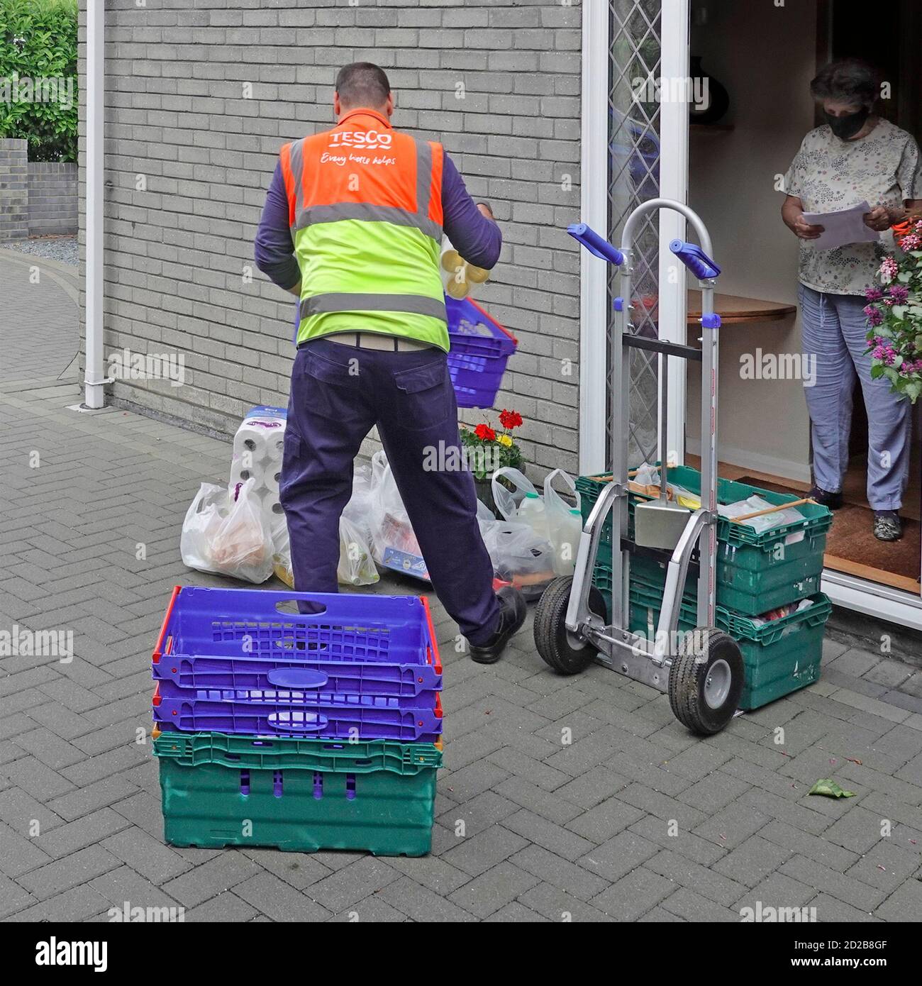 Tesco grocery food shopping in plastic bag delivery van driver & bags at front door maintains social distance customer wearing Covid 19 face mask UK Stock Photo