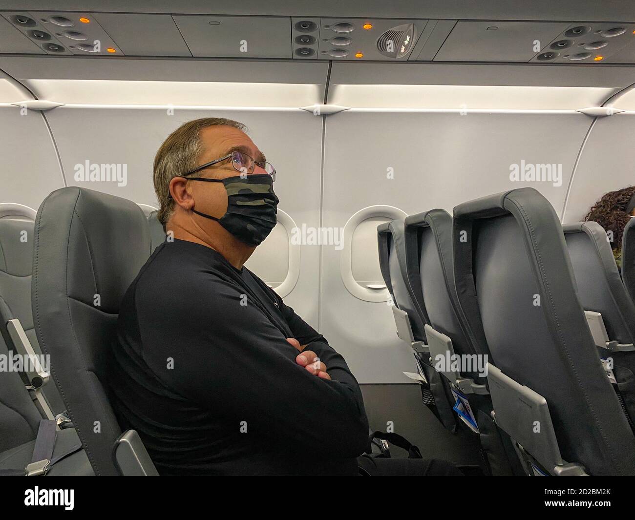A man wearing a face mask sitting on an airplane waiting for it to take