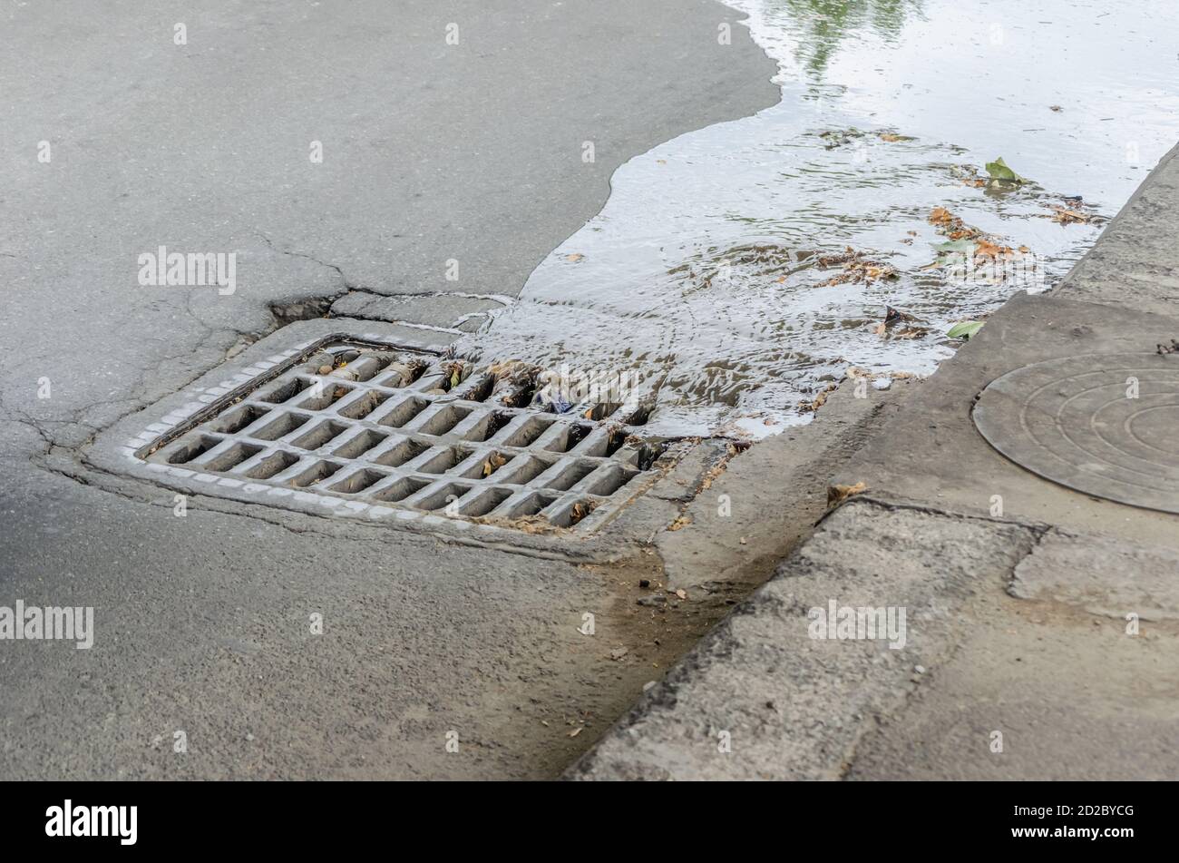 Water drains into a storm drain on the road close-up Stock Photo