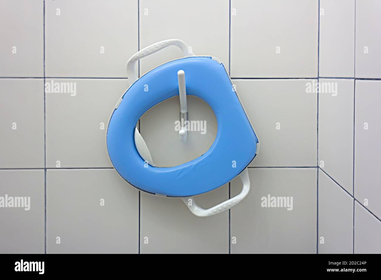 Blue child, toddler toilet seat hanging on a hook on a white ceramic tiles wall in an indoor WC, toilet room in a cafe Stock Photo