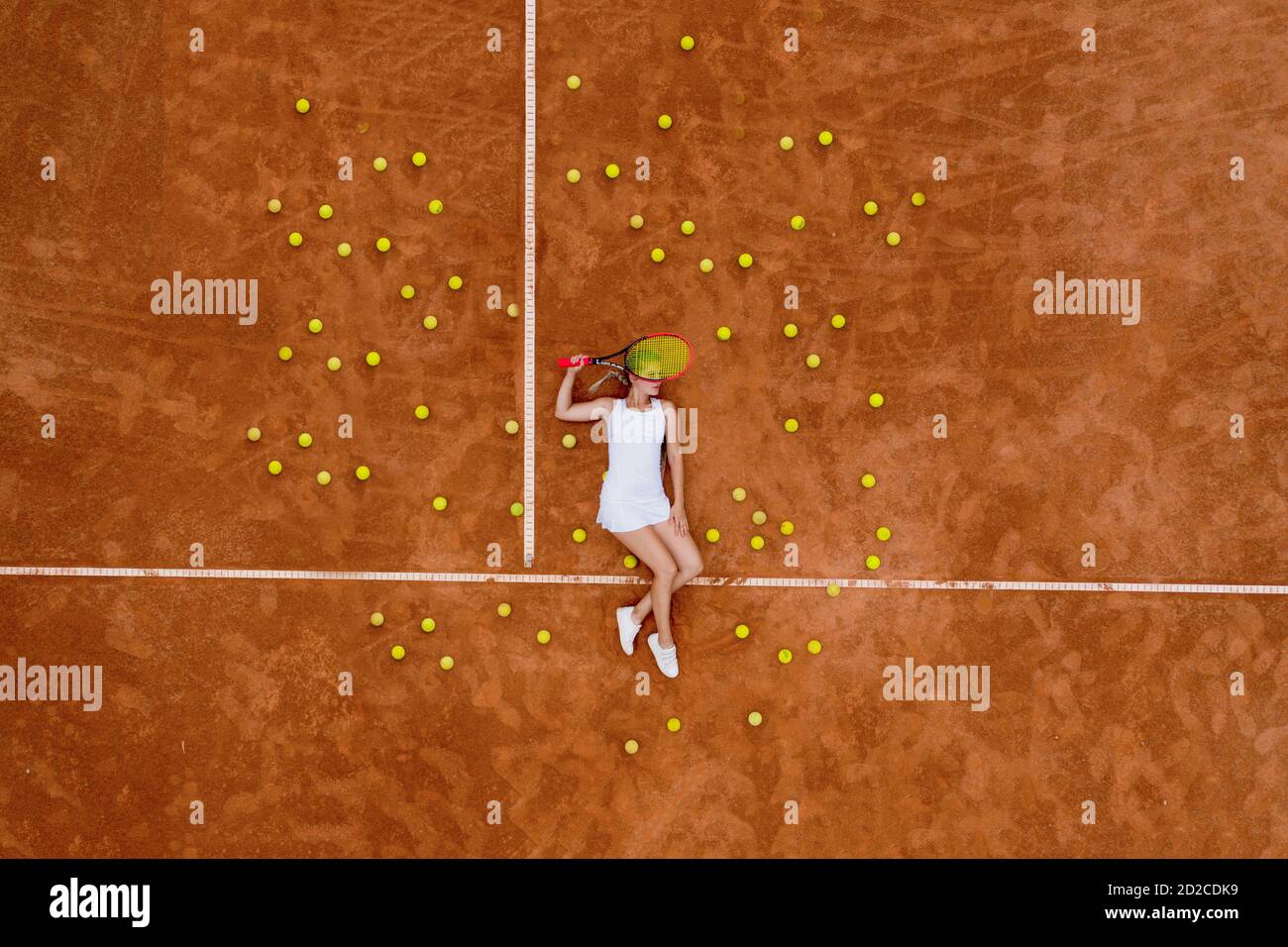 Portrait of smiling woman relaxing on tennis court with a lot of balls and racket after hard tennis trainingg outdoor. Dolly shot. Top view Stock Photo