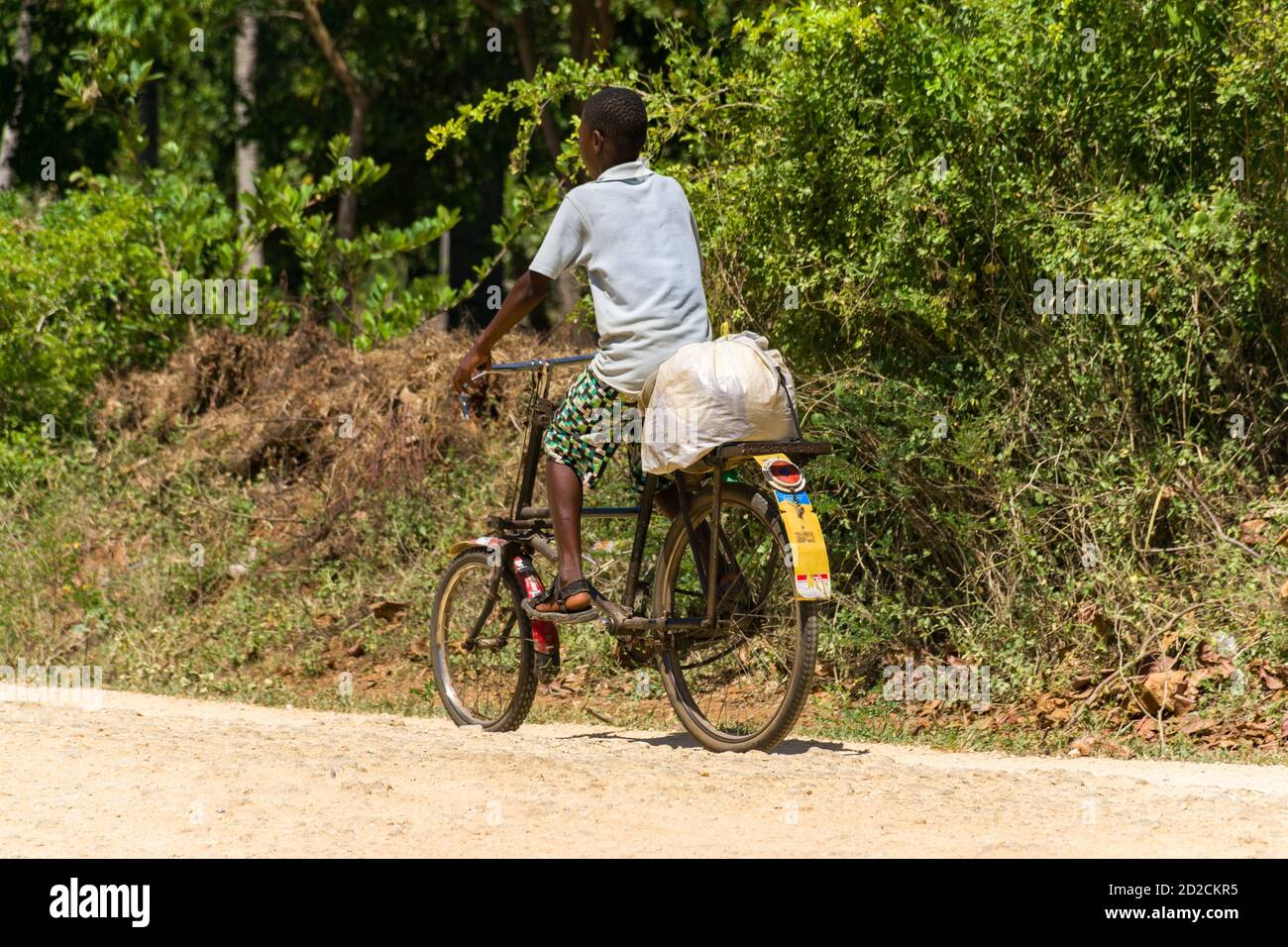 A Kenyan boy riding a bicycle on a dusty road transporting goods on the back, Kenya, East Africa Stock Photo