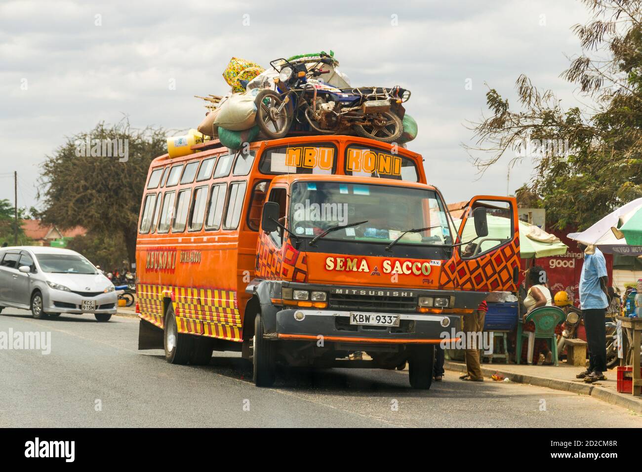 A bright orange bus stopped at bus stop loading passengers on Mombasa highway, Kenya, East Africa Stock Photo