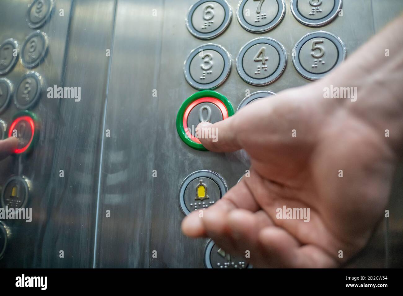 The thumb presses the button in the elevator zero floor close-up. The elevator buttons are signed in braille. The concept of inclusion. Stock Photo