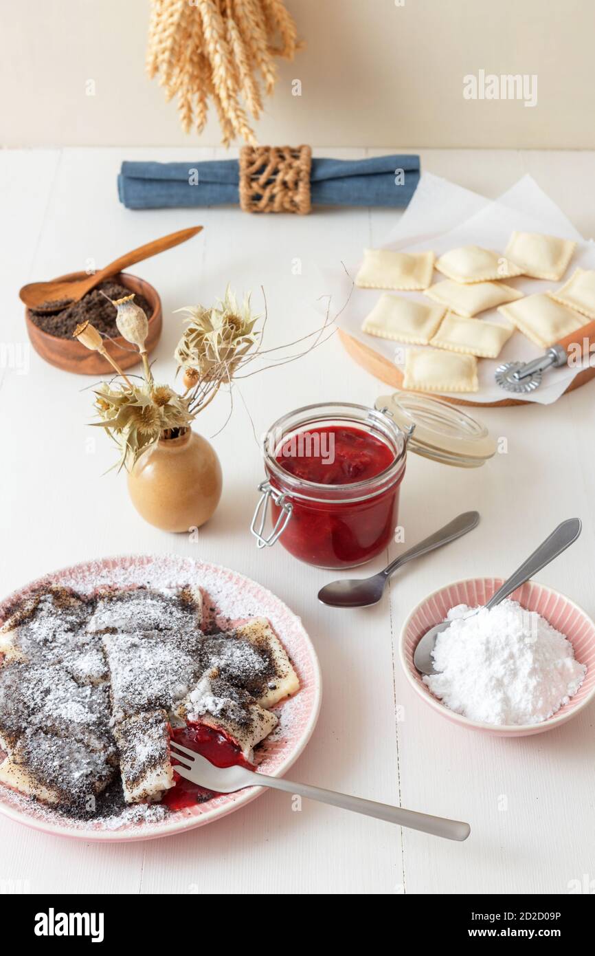 Pastry parcels filled with plum marmalade, dusted with poppy seed and icing sugar. Tasty poppy seed dessert or main course. White wooden table backgro Stock Photo