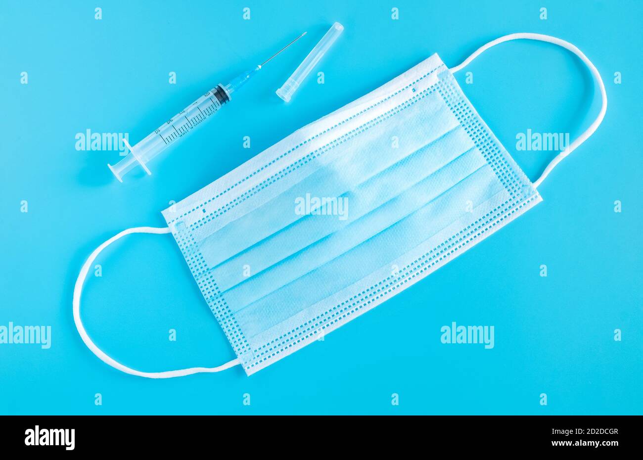 A blue medical mask and a disposable syringe on a light blue background
