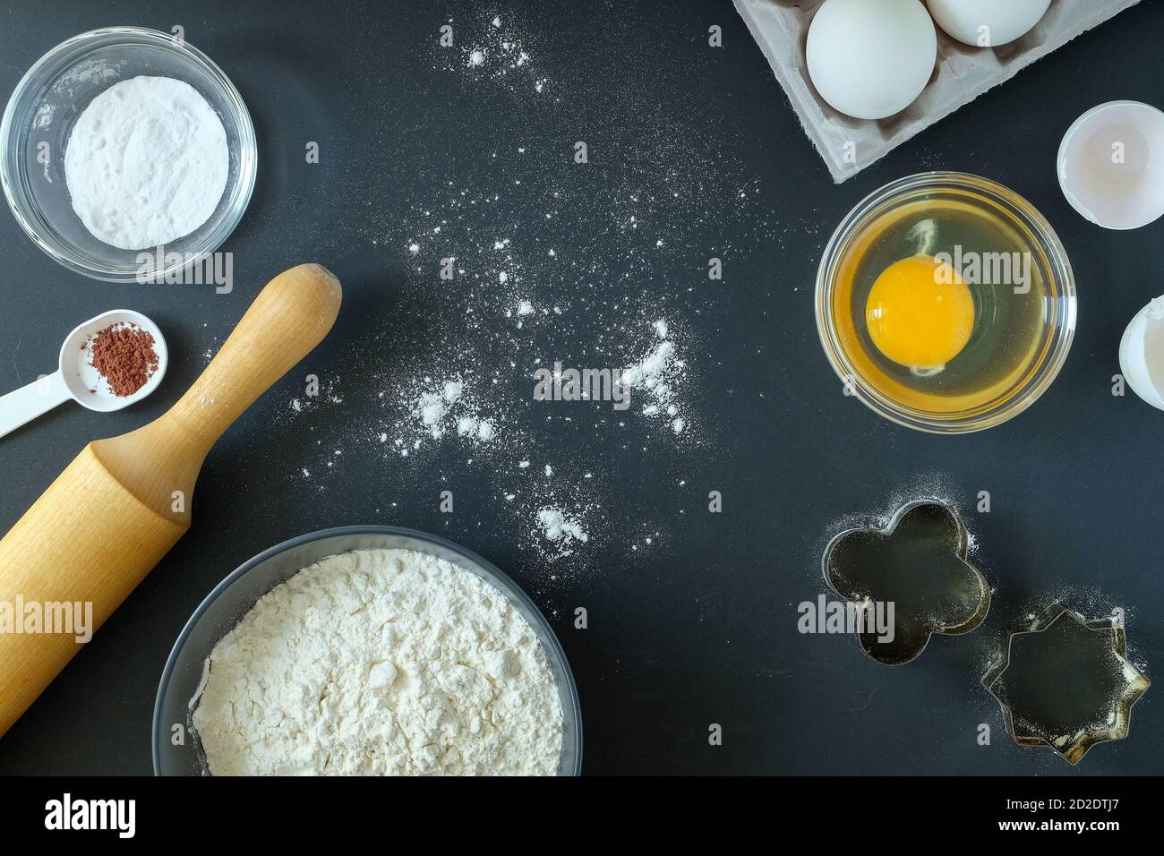 Flour, baking powder, cinnamon, eggs, cookie moulds and rolling pin on a black background Stock