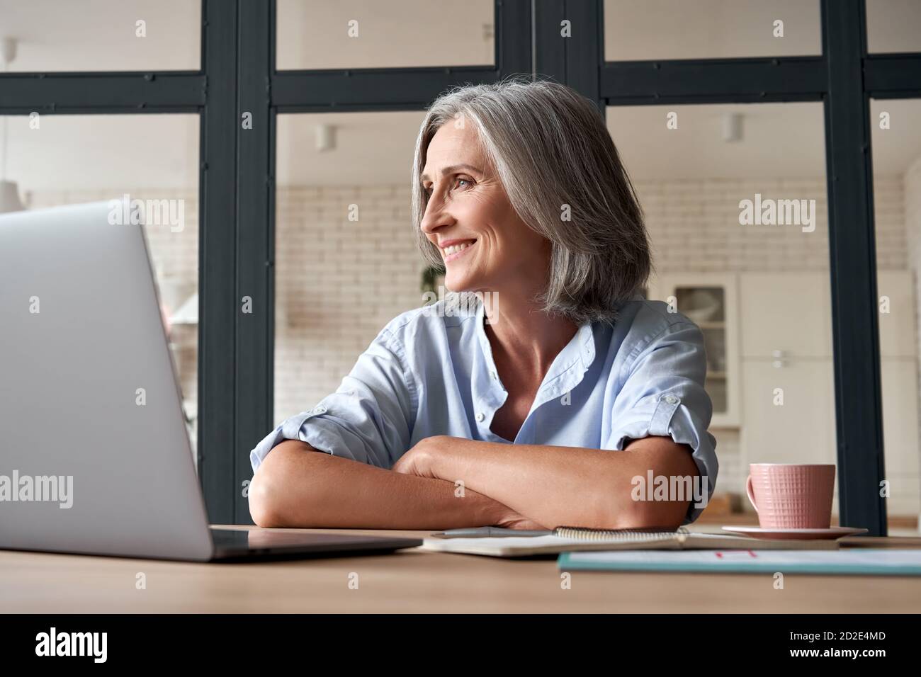 Smiling mature middle aged woman dreaming looking away at workplace. Stock Photo