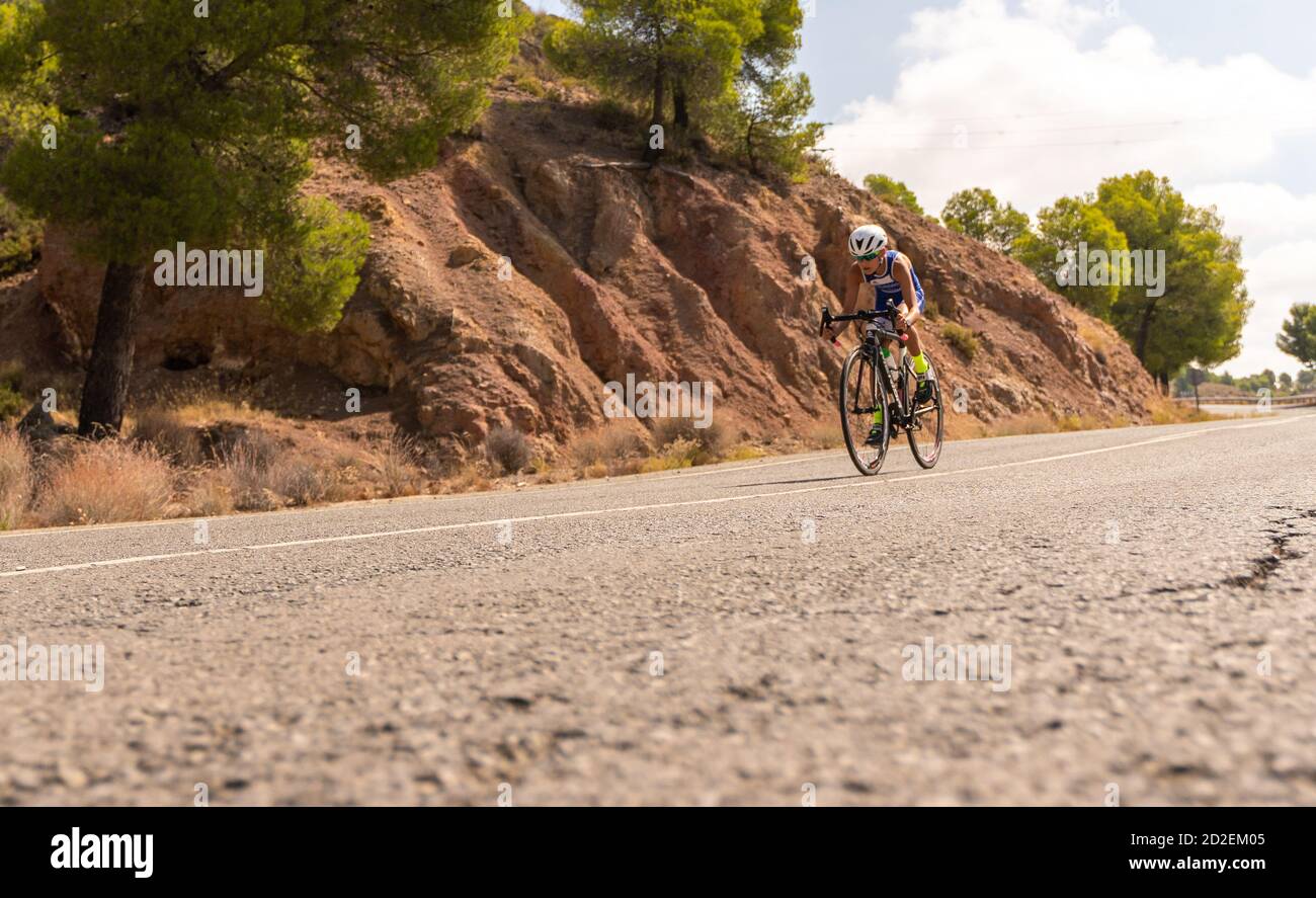 Boy cycling on a road bike outside on the road with trees in the
