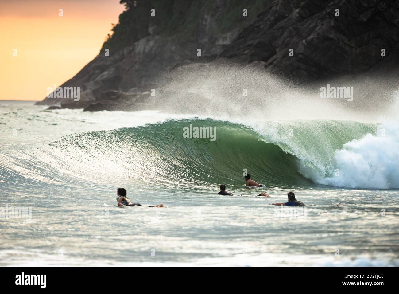 A wave breaks as surfers paddle out, at Santiago Beach, SE Brazil Stock Photo