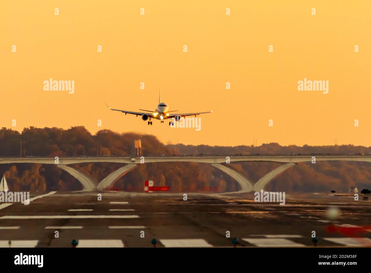 A passenger airline is slowly descending to land on a runway at sunset. The lights of the plane are on and wheels are down. There is scenic sunset sky Stock Photo