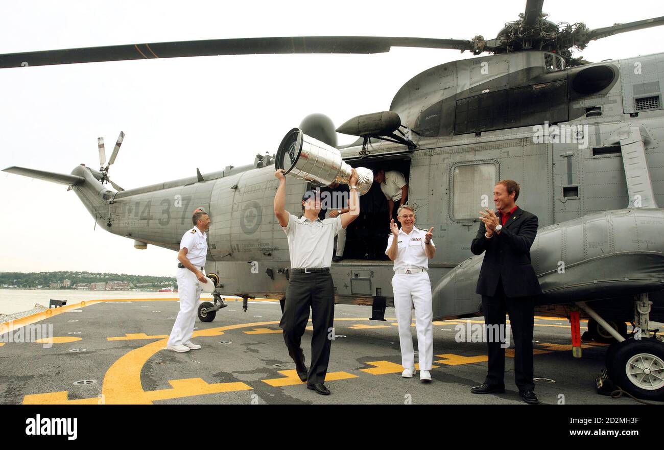 Pittsburg Penguins Captain Sidney Crosby carries the Stanley Cup from a Sea  King Helicopter and receives applause from Rear Admiral Paul Maddison (2nd  R) and Defense Minister Peter MacKay (R) shortly after