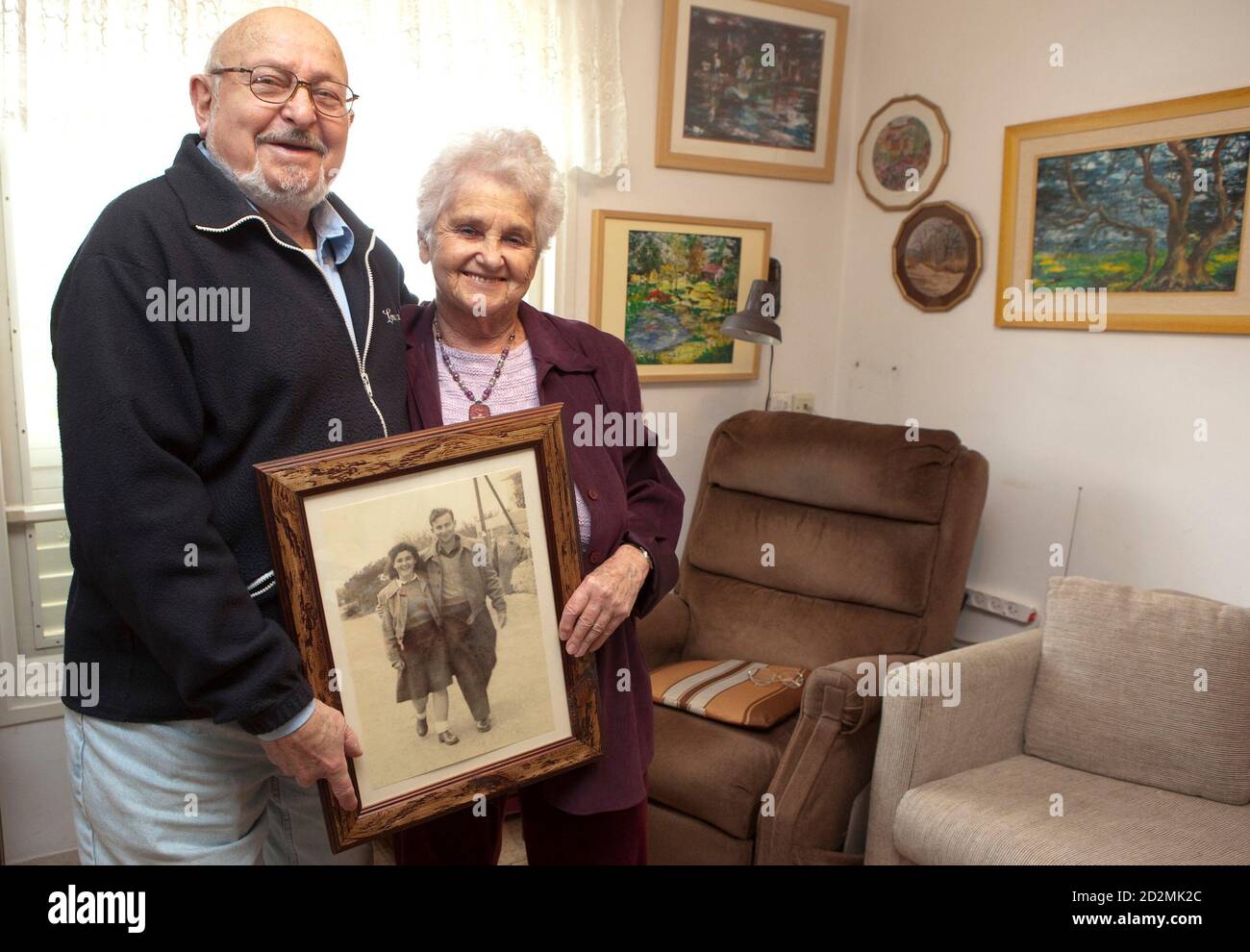 Holocaust survivors Yehudit (R) and Ezra Amit hold a photograph of themselves when they were younger, at their home in Kibbutz Shaar Haamakim in northern Israel April 9, 2010. The couple wed in British-ruled Palestine and currently have four children and seven grandchildren. Starting Sunday evening, Israel marks the annual memorial day commemorating the six million Jews killed by the Nazis in the Holocaust during World War Two. Picture taken April 9, 2010. REUTERS/Baz Ratner     (ISRAEL - Tags: ANNIVERSARY CONFLICT) Stock Photo