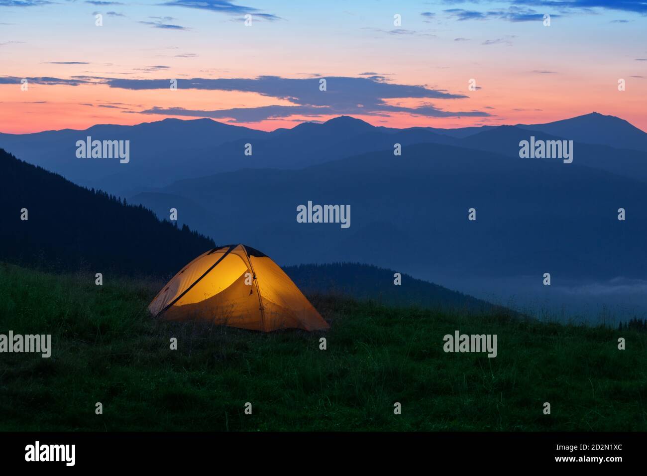 Orange tourist tent illuminated from inside on mountain Stock Photo