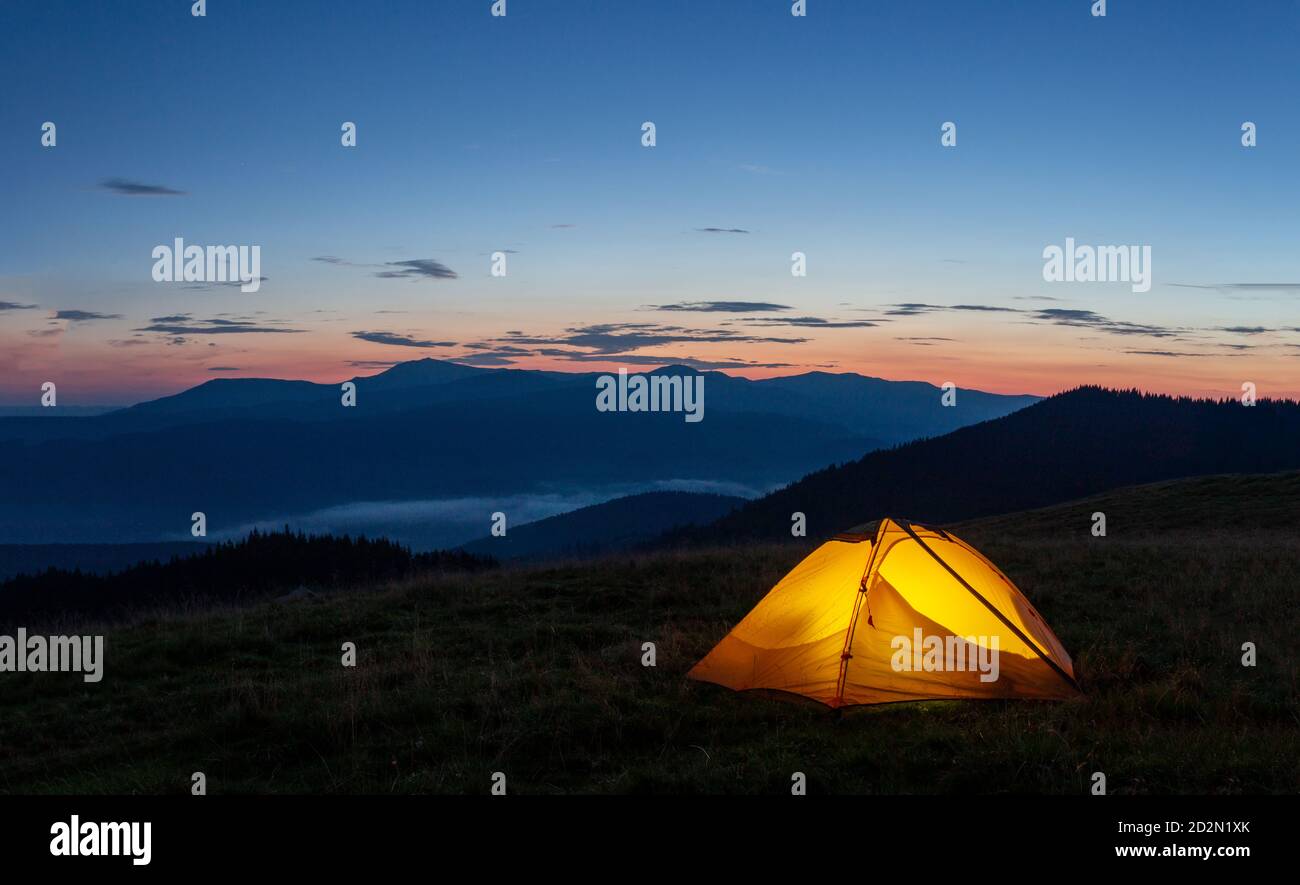 Orange luminous tent on the mountain in evening or early morning Stock Photo
