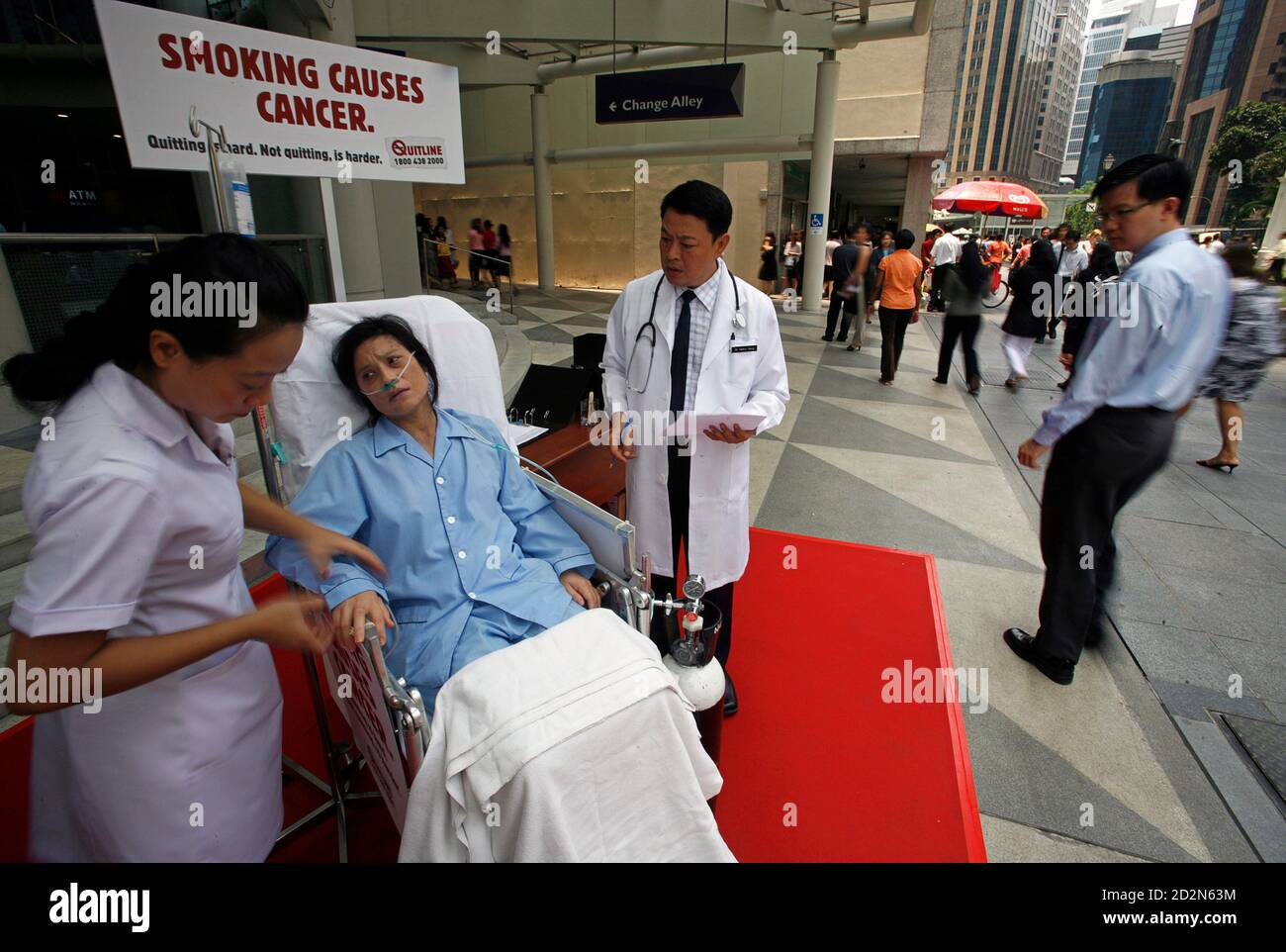 A woman dressed as a patient is attended to by people dressed as a doctor and a nurse as lunchtime crowds walk past in Singapore's financial district March 28, 2007. The scene is part of the three-month long "Smoking Control Campaign" launched by Singapore's Health Promotion Board last week. REUTERS/Vivek Prakash (SINGAPORE) Stock Photo