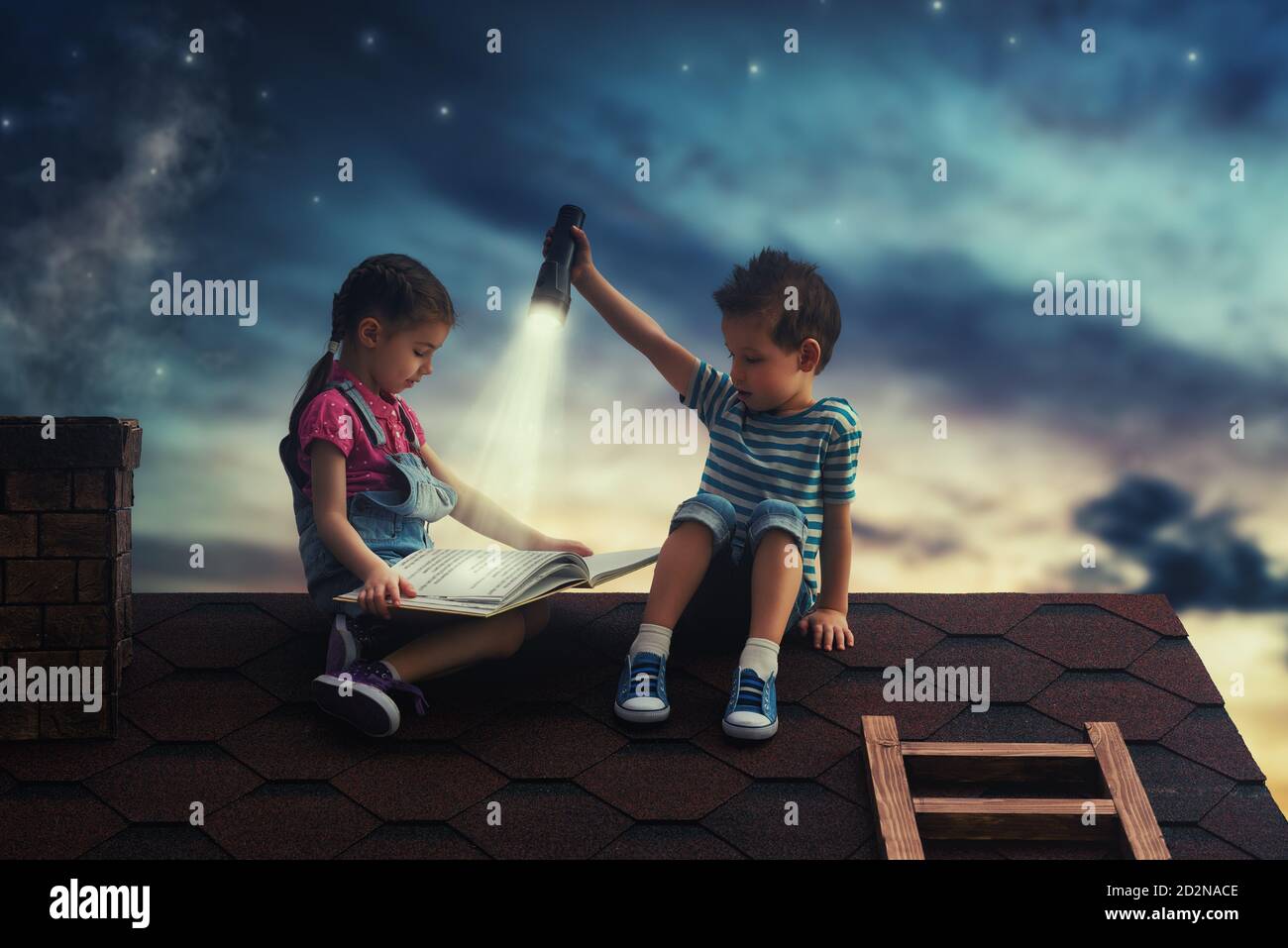 Children reading a book sitting on the roof of the house. Boy and girl ...