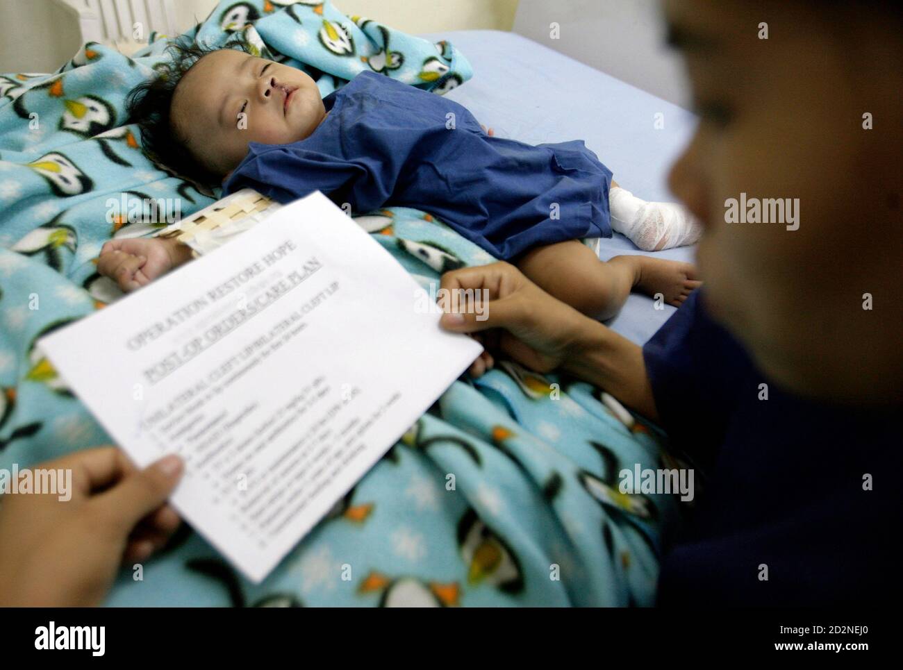 A boy, inflicted with a cleft lip, lies on a hospital bed after surgery as his mother reads the post-operation care plan during 'Operation Restore Hope' at Diosdado Macapagal Memorial Medical Center in Caloocan City, Metro Manila April 12, 2010. Operation Restore Hope, a group of medical volunteers from Germany, New Zealand and Australia who perform surgeries for underprivileged children every year, aim to provide free surgery for about 70-80 children inflicted with cleft lips, cleft palates, and other facial deformities over a period of five days. REUTERS/Cheryl Ravelo (PHILIPPINES - Tags: HE Stock Photo