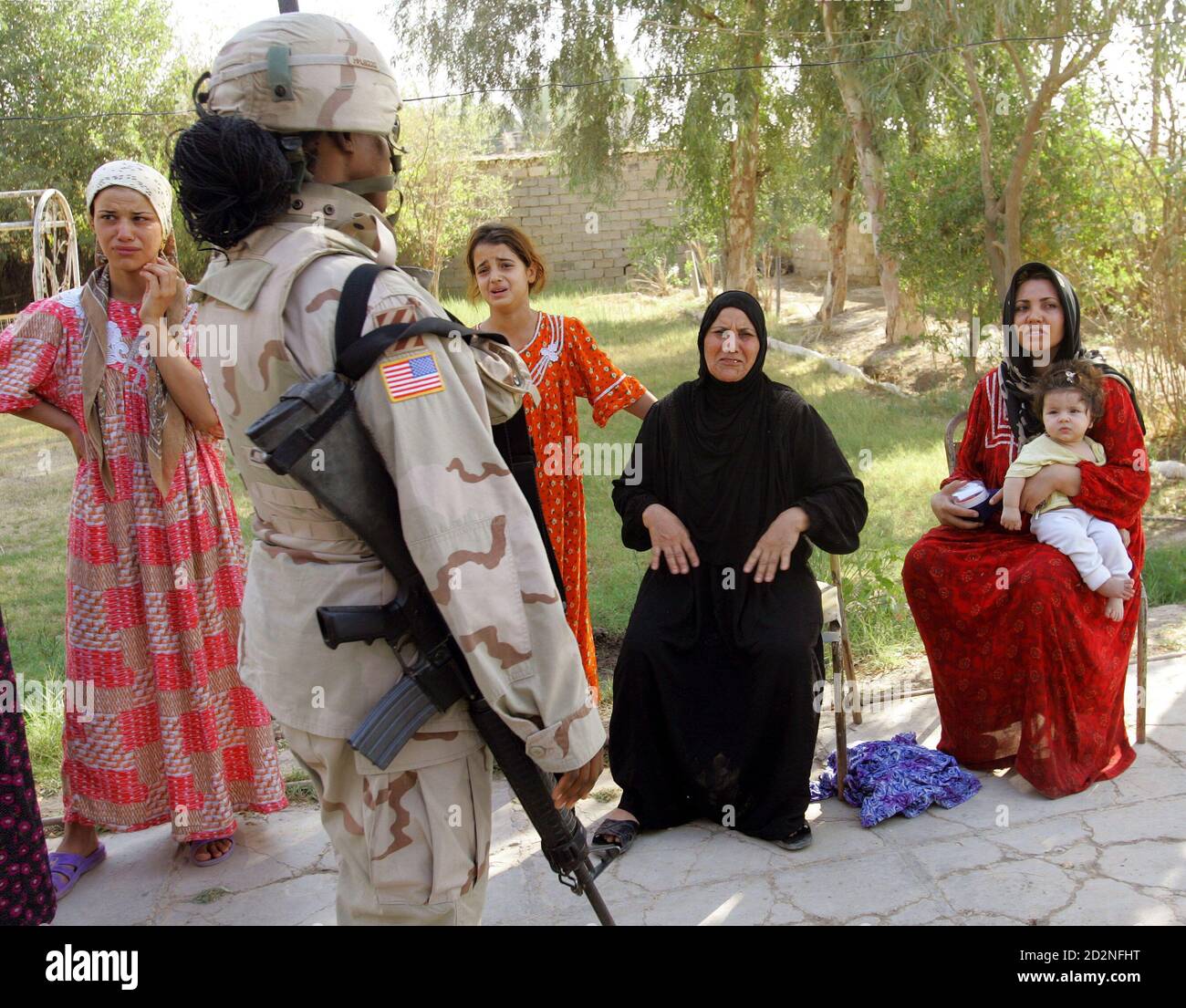 A female U.S. soldier of the 3rd battalion, 7th Infantry, 4th Brigade, 3rd Infantry Division from Ft Benning, Georgia guards crying women after a family member was detained during a raid searching for illegal weapons inside their house in Baghdad August 3, 2005. Fourteen Marines were killed in a roadside bomb blast in western Iraq on Wednesday, the U.S. military said, in one of the single deadliest attacks against U.S. forces since the beginning of the war. REUTERS/Andrea Comas  ACO/SA Stock Photo