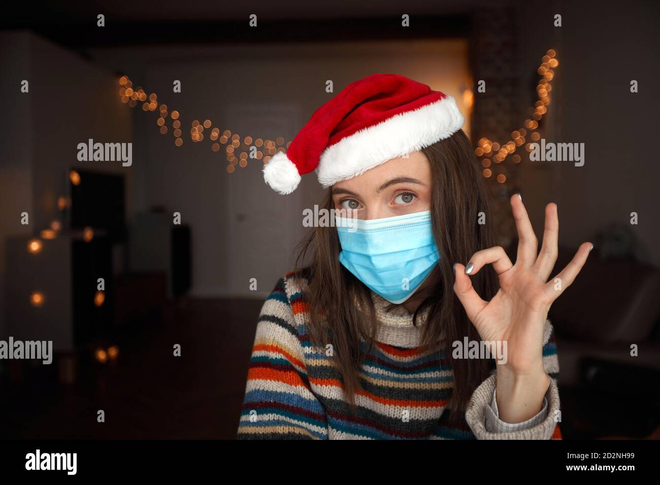 Cheerful woman in medical mask showing OK gesture on Christmas day Stock Photo
